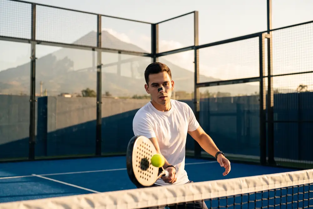Un hombre juega pádel al atardecer con la tira VENTUS Nariz puesta; al fondo, el volcán.